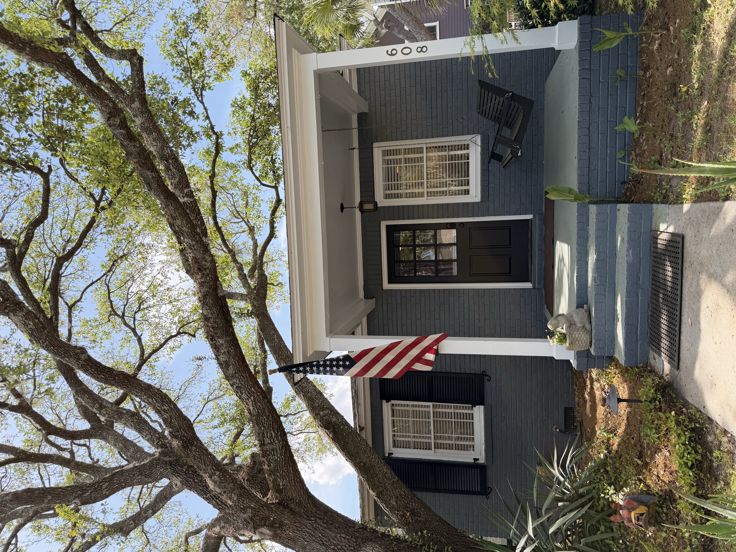608 Bladen Street — a charming gray brick cottage with black shutters and a welcoming front porch, shaded by a grand live oak tree in Beaufort's Historic District